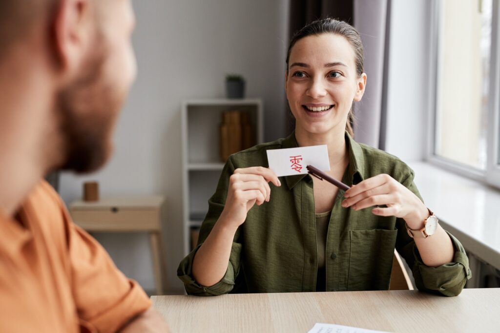 Young smiling female tutor pointing at paper card with Chinese hieroglyph